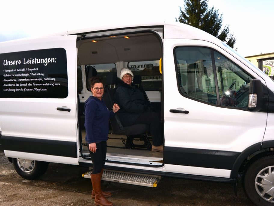 Frau steht neben einem weißen Transportwagen, eine Person sitzt im Inneren.