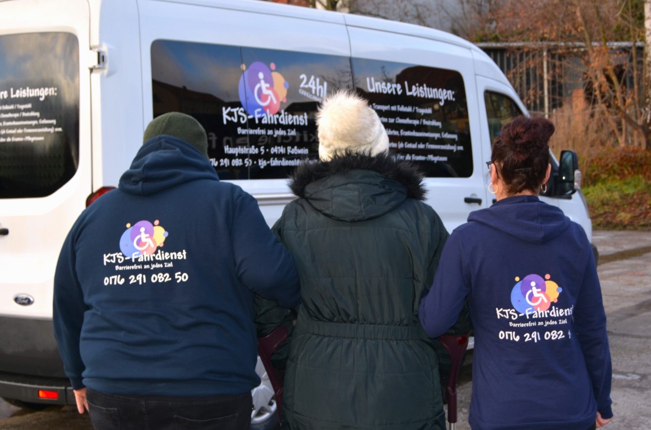 Hilfsbedürftige Personen wird von zwei Mitarbeitern zum Auto begleitet.
